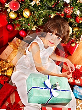 Child with gift box near Christmas tree.