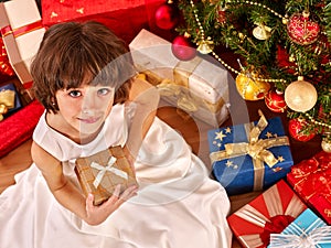 Child with gift box near Christmas tree.