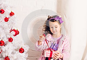 Child with gift box near white Christmas tree
