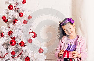 Child with gift box near white Christmas tree