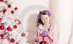 Child with gift box near white Christmas tree