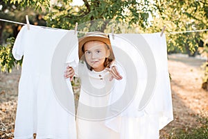Child girl 5-6 year old wear dress and straw hat playing with bed sheets on rope outdoor.