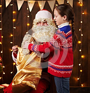 Child girl accepting gifts from Santa near decorated xmas tree with lights, they talking and smiling - Merry Christmas and Happy