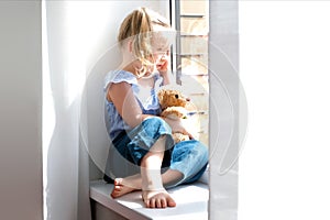 Child is a girl alone at home. Girls sitting on the windowsill and crying