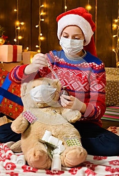 Child girl as Santa helper posing in new year decoration. Wearing a protective face mask against viruses, coronaviruses. She plays