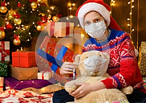 Child girl as Santa helper posing in new year decoration. Wearing a protective face mask against viruses, coronaviruses. She plays