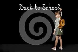 Child girl with backpack writing on the blackboard with brush. Back to school, study, education, success concept