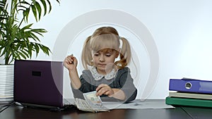 Child girl boss counting dollar cash bills. Baby businesswoman kid with money is sitting at office