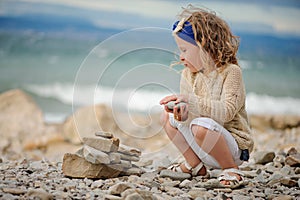 Child girl building stone tower on the beach in summer day