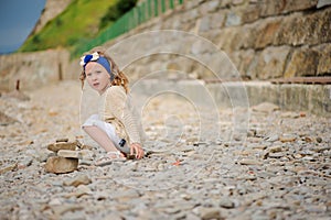 Child girl building stone tower on the beach in summer day