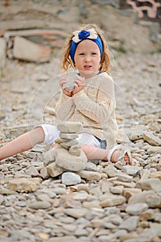 Child girl building stone tower on the beach in summer day