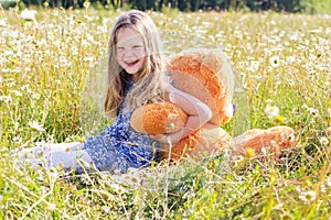Child girl in camomile field with teddy bear