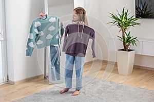 Child Girl Choosing Between Two Sweaters at Home. Morning preparation before school