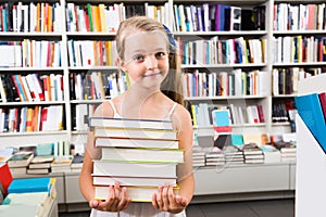 Child girl chose a lot of books in the library