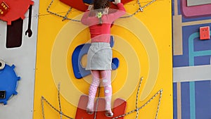Child girl climbing up on an indoors climbing wall. Baby plays children`s sports games on the playground