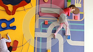 Child girl climbing up on an indoors climbing wall. Baby plays children`s sports games on the playground