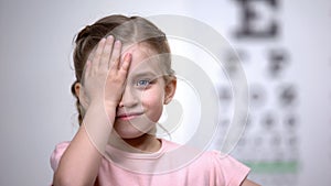 Child girl closing eye, showing size or sign from eye chart, vision diagnostics