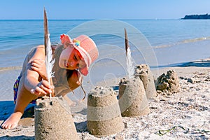 Child girl decorates sand towers, figure with seagull feathers