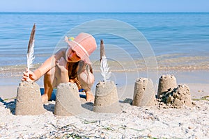 Child girl decorates sand towers, figure with seagull feathers