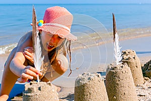 Child girl decorates sand towers, figure with seagull feathers