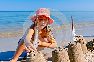 Child girl decorates sand towers, figure with seagull feathers