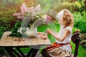 Child girl decorating cakes with flowers on garden tea party in spring