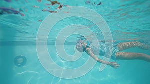 Child girl diving underwater in snorkeling mask in pool, dog looking after her.