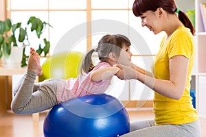 Child girl doing gymnastic on fitness ball with mother at home