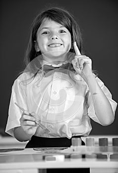 Child girl draws in classroom sitting at a table, having fun on school blackboard background. Portrait of little girl