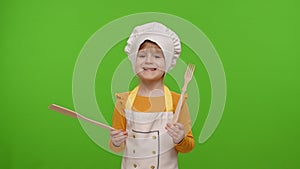Child girl dressed in apron like chef cook dancing with fork and spatula on chroma key background