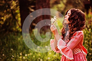 Child girl dressed as fairytale princess playing with blow ball in summer forest