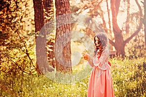 Child girl dressed as fairytale princess playing with blow ball in summer forest