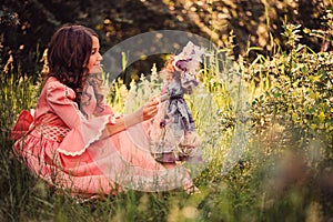 Child girl dressed as fairytale princess playing with doll in summer forest