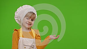 Child girl dressed like chef cook pointing at right on blank space place for your advertisement logo