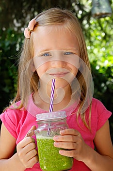 Child girl drinking healthy green vegetable smoothie - healthy eating, vegan, vegetarian, organic food and drink concept