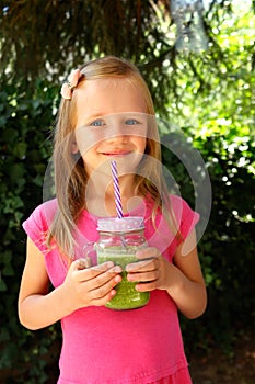 Child girl drinking healthy green vegetable smoothie - healthy eating, vegan, vegetarian, organic food and drink concept