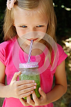 Child girl drinking healthy green vegetable smoothie - healthy eating, vegan, vegetarian, organic food and drink concept