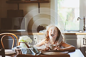 Child girl drinking tea for breakfast in summer country kitchen