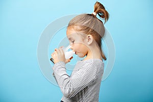 Child girl drinks milk without lactose, sideways portrait against blue isolated.