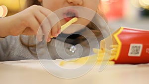 Child girl eating fast food french fries in a cafe. Portrait closeup.