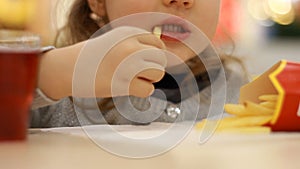 Child girl eating fast food french fries in a cafe. Portrait closeup.