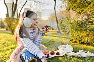 Child girl eating fresh red apples in sunny autumn park