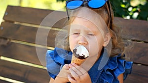 Child girl is eating ice cream while sitting on a bench in the park on a sunny summer day. Portrait of a baby close-up.