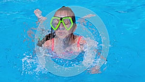 Child girl emerges from pool water. Girl dives and swims in a pool with clear blue water. Summer vacation concept. Slow