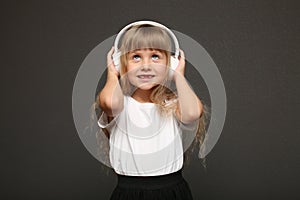 child girl enjoys music in her big white headphones and smile.Blue eyes blonde hair girl listen to music
