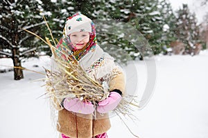 Child girl in a fur coat and in a scarf in Russian style with a bunch of brushwood