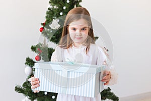 Child girl with gift box near Christmas tree. Holidays, christmas time and presents concept.