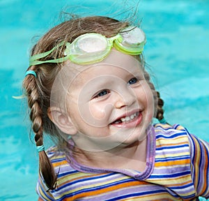 Child girl in goggles swimm pool.