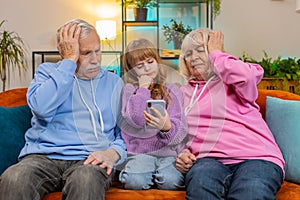Child girl granddaughter grandfather grandmother playing game on smartphone losing fail at home