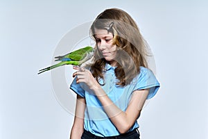 Child girl with green quaker parrot looking at pet on light studio background